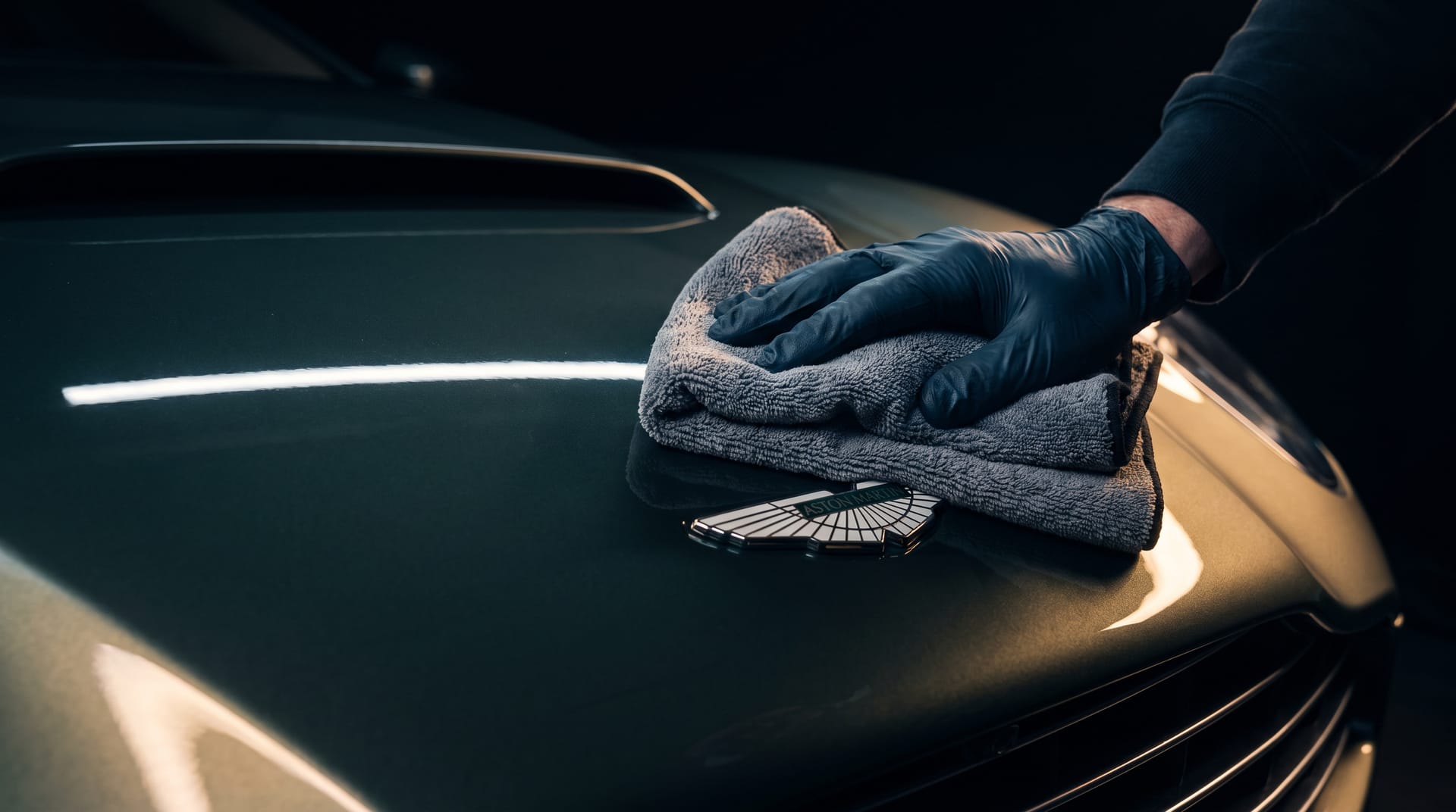 Hand met microvezeldoek polijst het Aston Martin-embleem op een donkergroene motorkap
