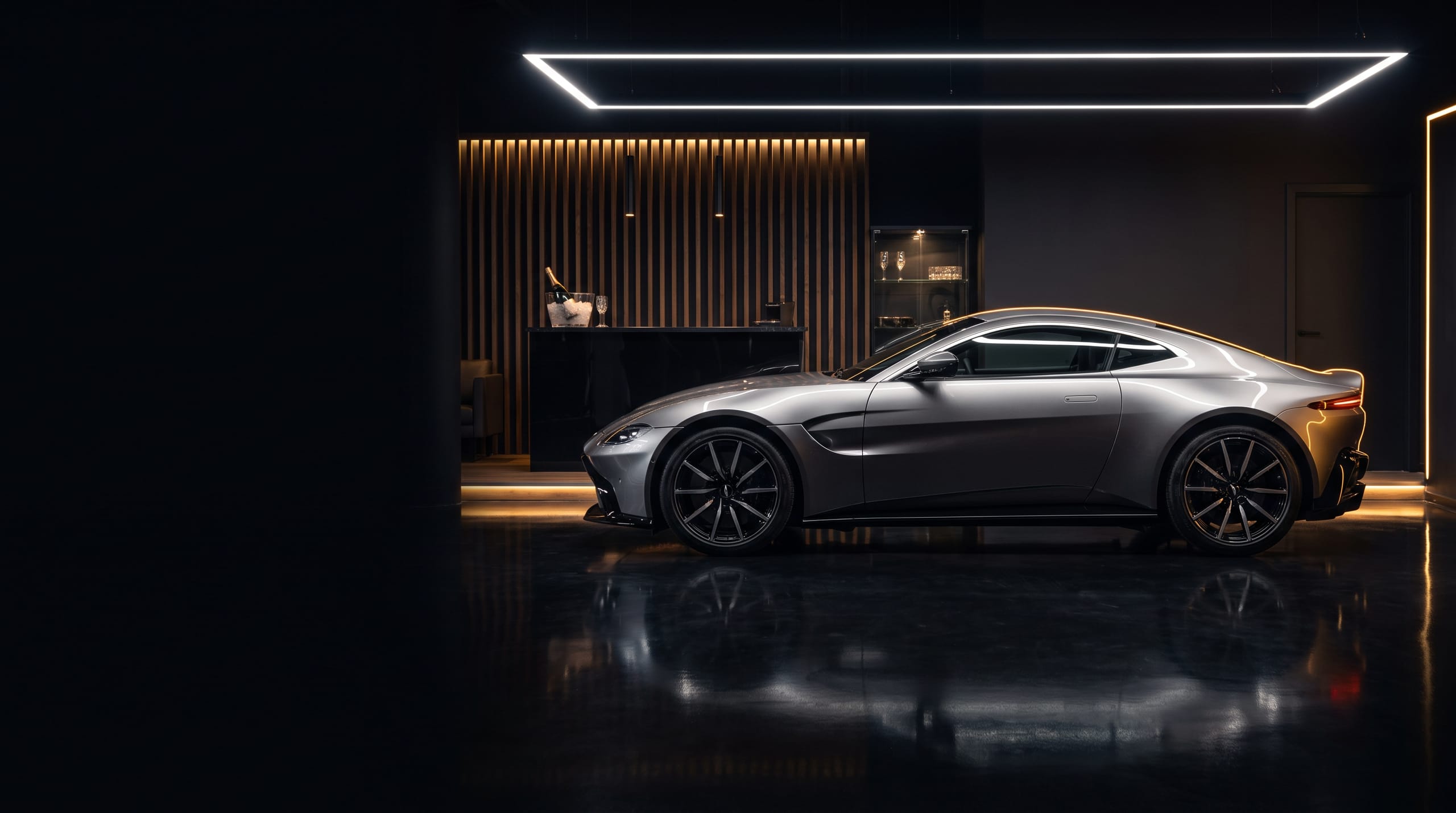 Aston Martin Vantage in zilver in de studio met de verlichte lounge van GT Exclusive op de achtergrond